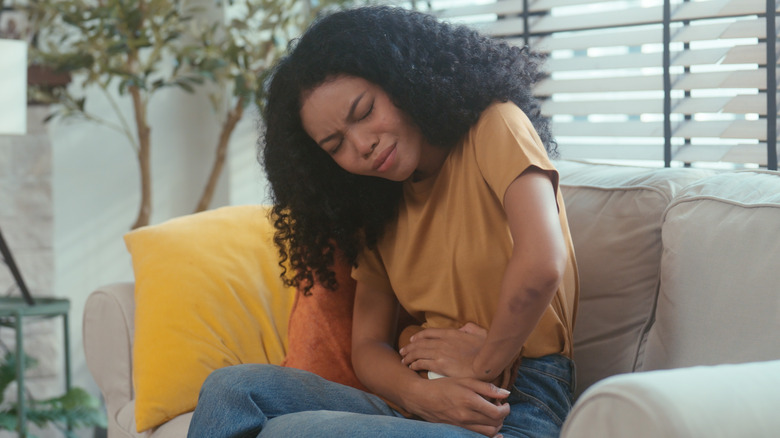 woman sitting on couch clutching stomach in pain