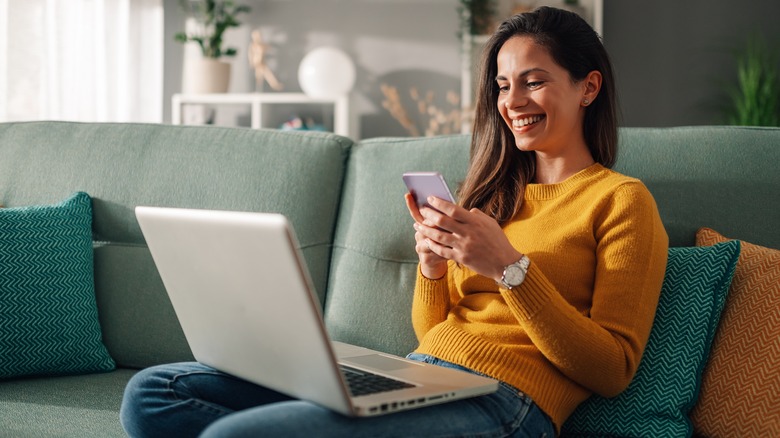 woman smiling at phone with laptop on lap