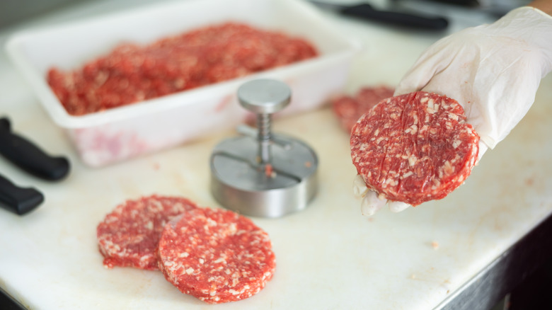 Gloved hands holding raw beef patty