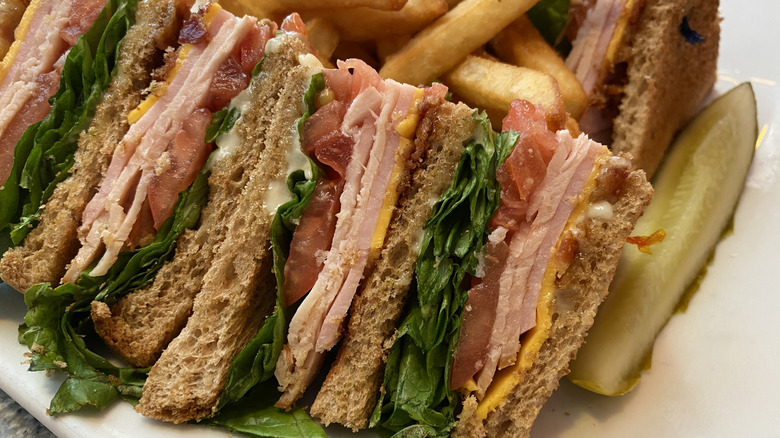 Club sandwich on a plate with pickle and fries