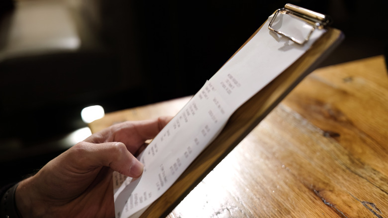 A hand holding a restaurant bill on a clipboard