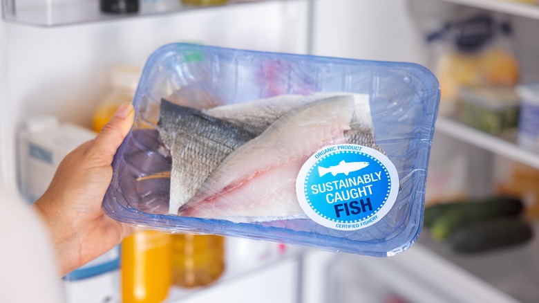 hand holds packaged fresh tilapia in front of open fridge