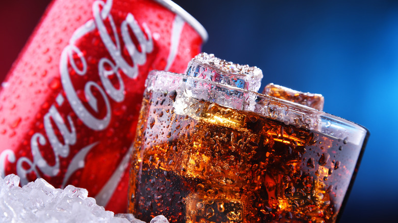 A red can of Coca-Cola next to a glass of Coke with ice