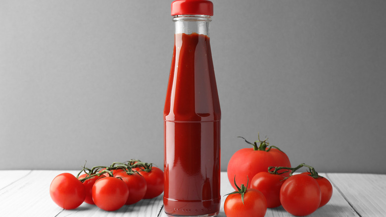 A bottle of ketchup and fresh tomatoes on a white table