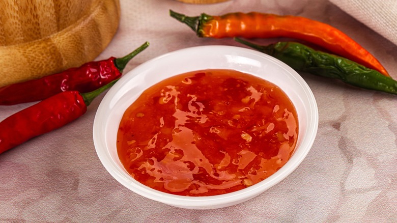 A bowl of sweet chili sauce surrounded by chili peppers