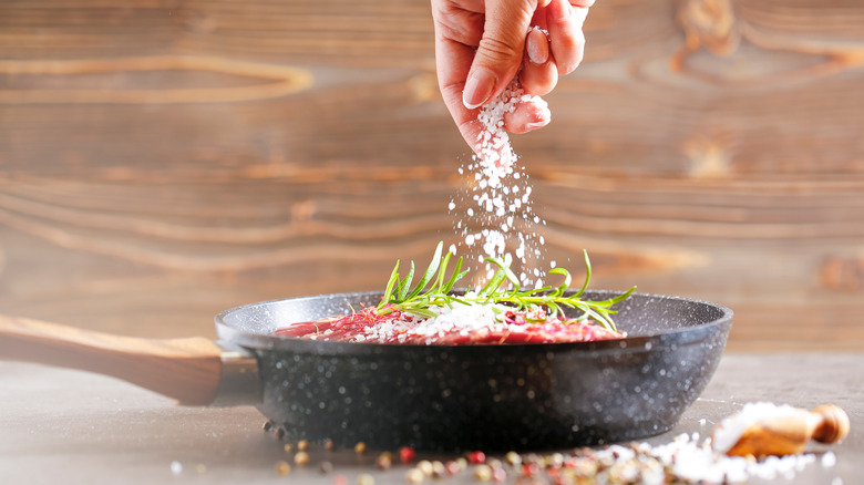 A hand adding salt to a steak