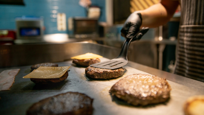 Person pressing burger into cooktop with spatula