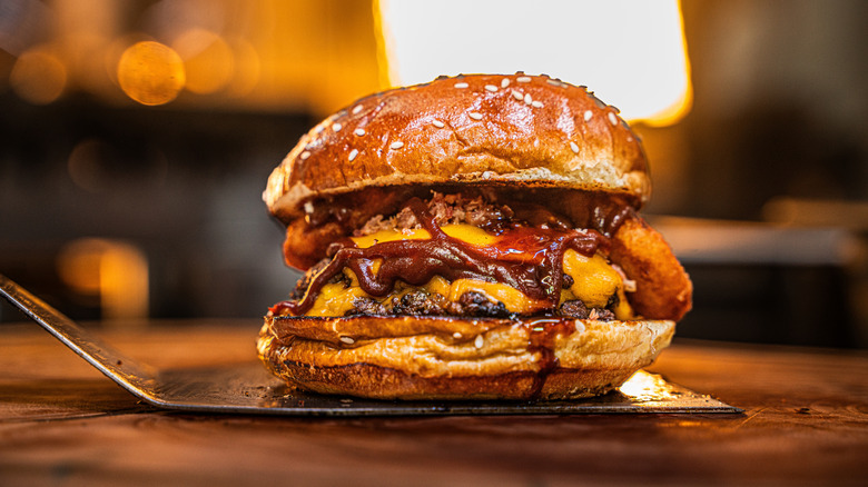 Large burger with lots of toppings on spatula