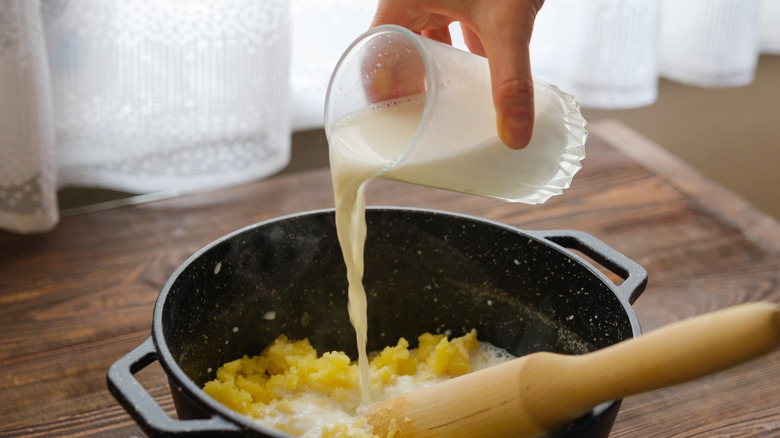 Milk being poured into a pot of mashed potatoes