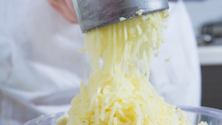 Person squeezing the handle of a ricer to break up a potato