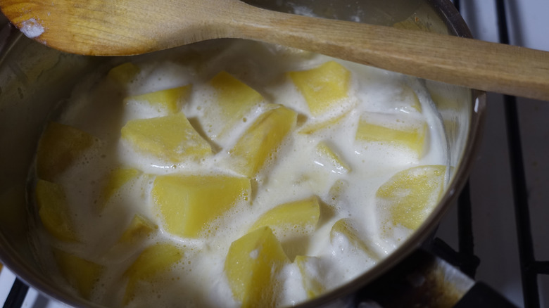 Potato pieces cooking in milk with a wooden spoon