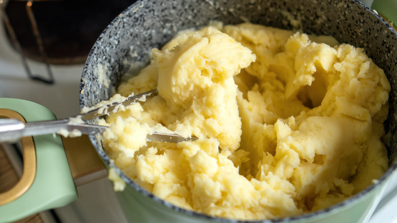 A hand masher in a bowl of mashed potatoes