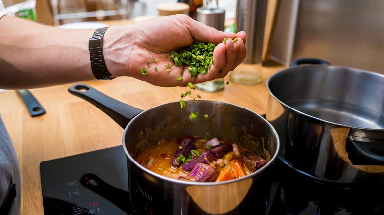 man adding herbs to sweet potato dish in skillet