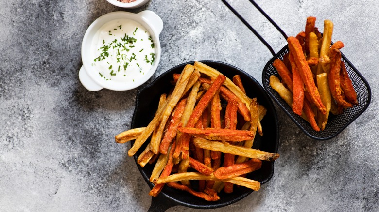 sweet potato fries in cast iron skillet and draining basket with dip