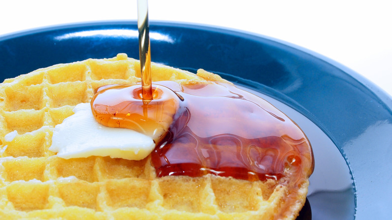 Maple syrup drizzling over buttered round waffle