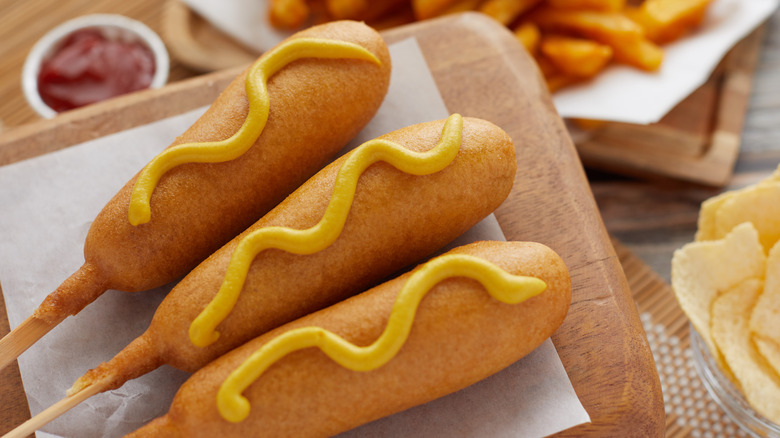 Corn dogs with mustard swizzle on wooden cutting board