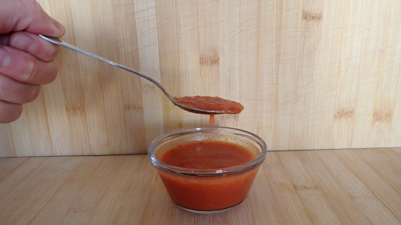 A hand with a spoonful of tomato soup above a bowl