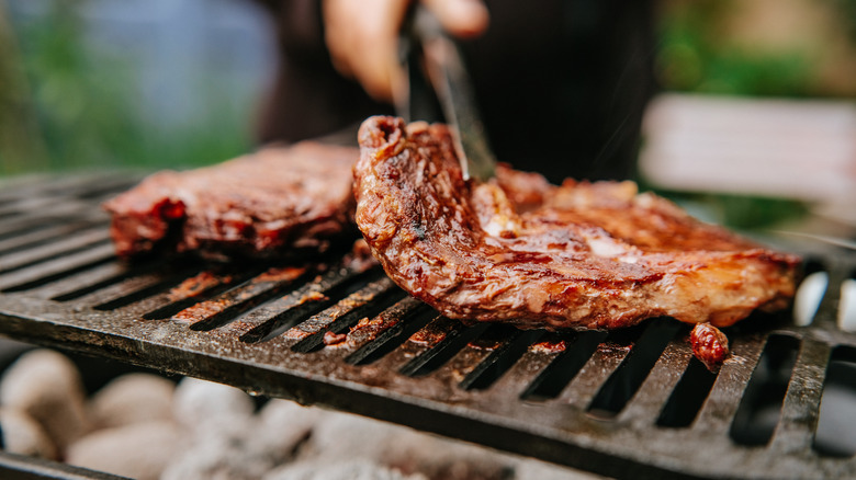 Hand flipping steaks on grill