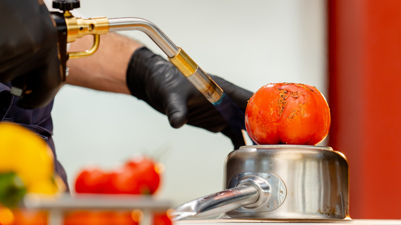 person blistering tomatoes on upside down steel pot with torch