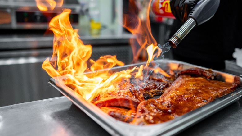 charring meat with a blow torch in a metal pan