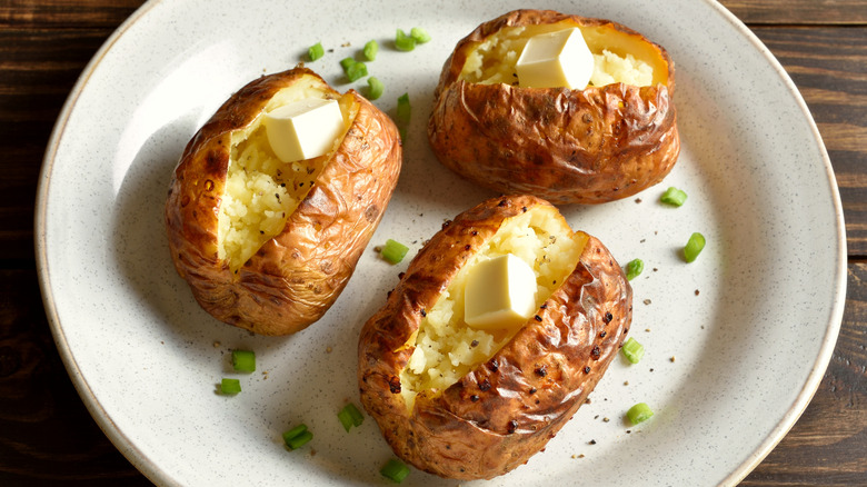 three baked potatoes with butter and crispy browned skins on plate