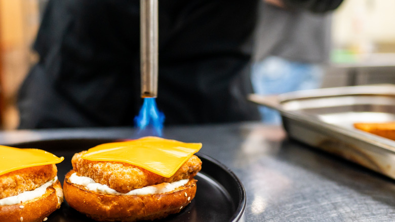 person blow torching cheese on fish sandwich