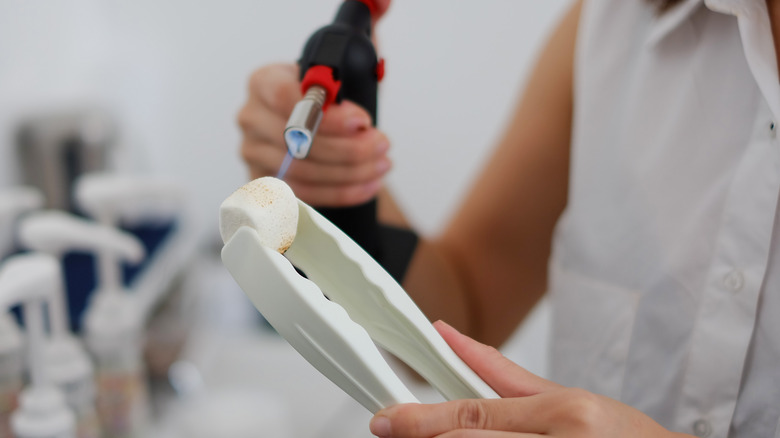 woman torching marshmallow held in white tongs