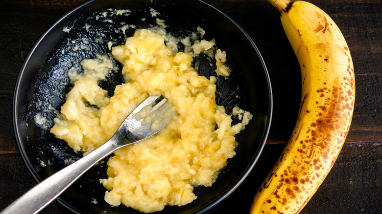 Mashed banana in a bowl next to one banana