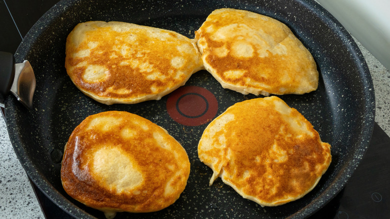 Person cooking four pancakes in skillet