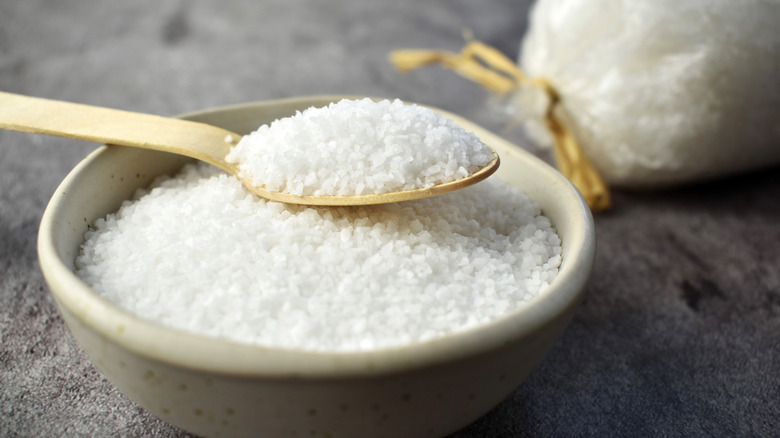 A wooden spoon of coarse salt in a bowl of salt