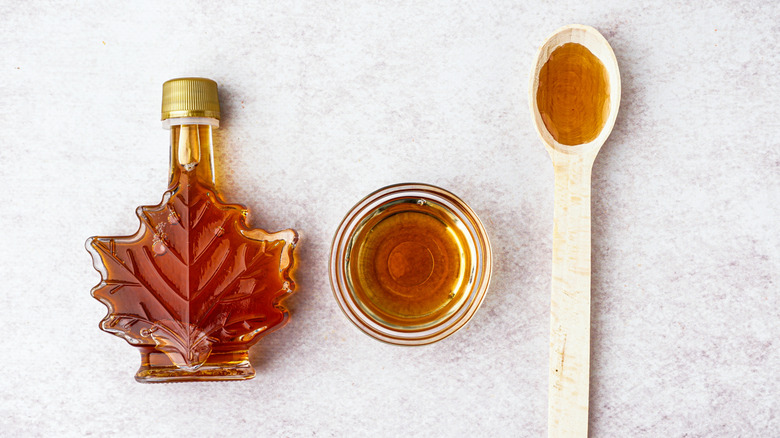 Maple syrup in bottle, glass ramekin, and wooden spoon