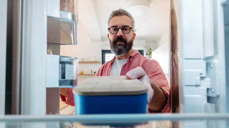 Man putting container of food in fridge