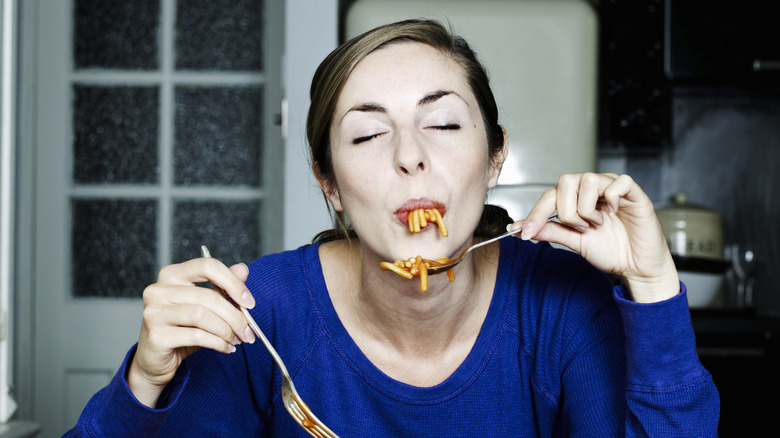 Woman eating pasta in kitchen