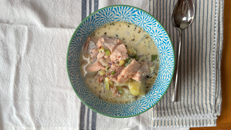 Bowl of salmon chowder on dish towel with spoon