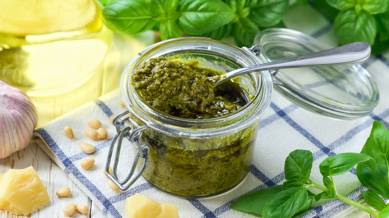 Pesto in glass jar with spoon surrounded by basil leaves