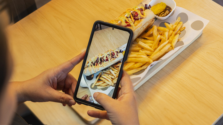 Person taking photo of fast food sandwich and fries