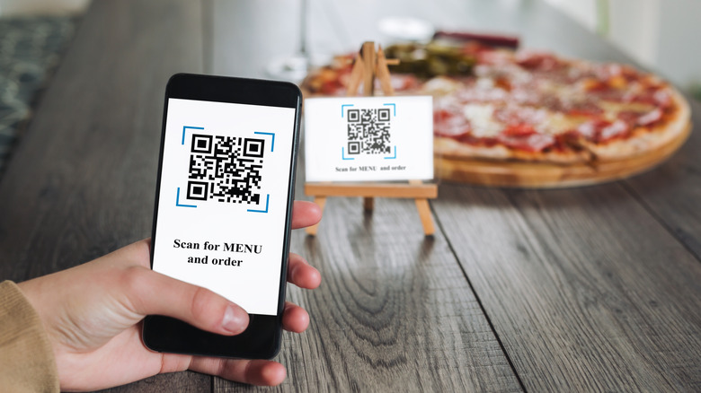 Phone held out to QR code with pizza in background