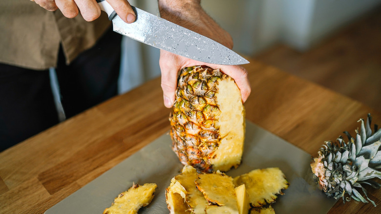 A person cutting pineapple with a large knife