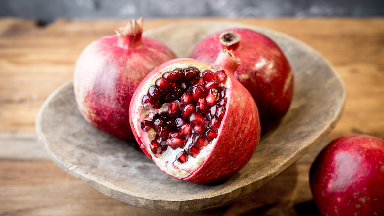 A wooden bowl of pomegranates, with one cut open