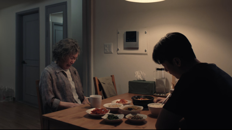 Hwang Jun ho and his mother sit across from each other at a table filled with sides and noodles