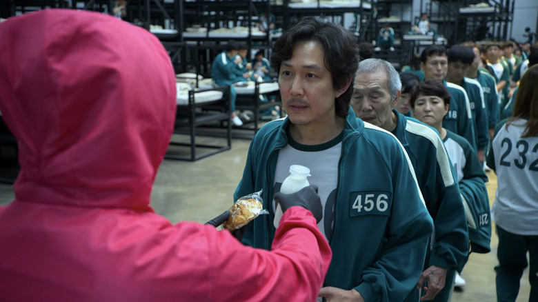 A guard in a pink uniform hands Gi-Hun his bun and bottle of milk