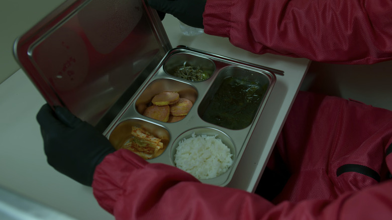 A tray with a multitude of foods in separate compartments being opened by a guard