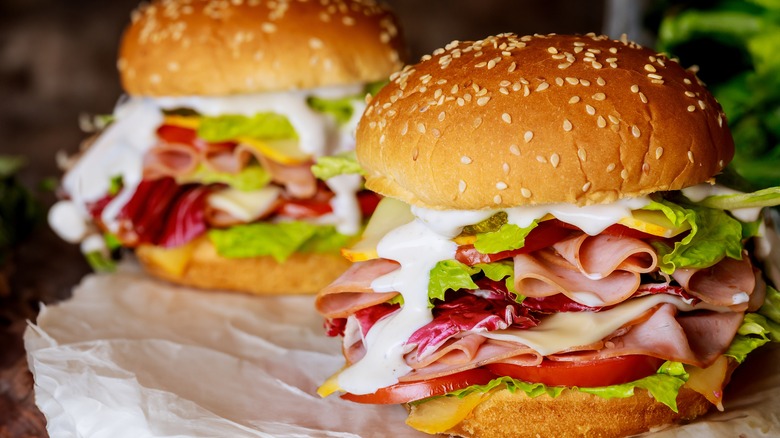 Sandwich piled with ingredients, including ham, cheese, lettuce, and ranch