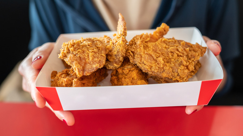 Hands holding container of fried chicken