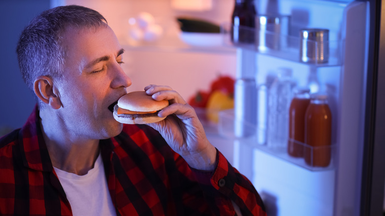 Person eating fast food by open fridge