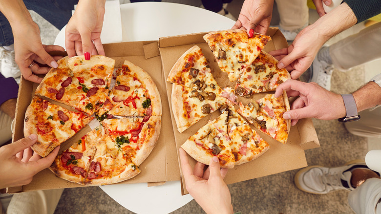 Hands taking pizza slices from box