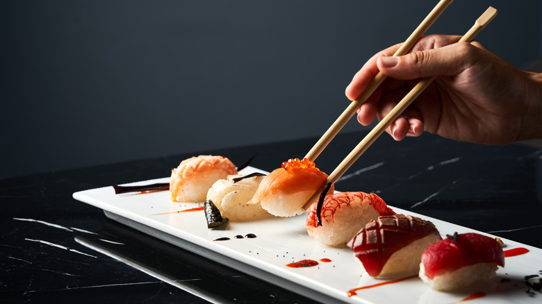 Hand with chopsticks grabbing sushi from white plate