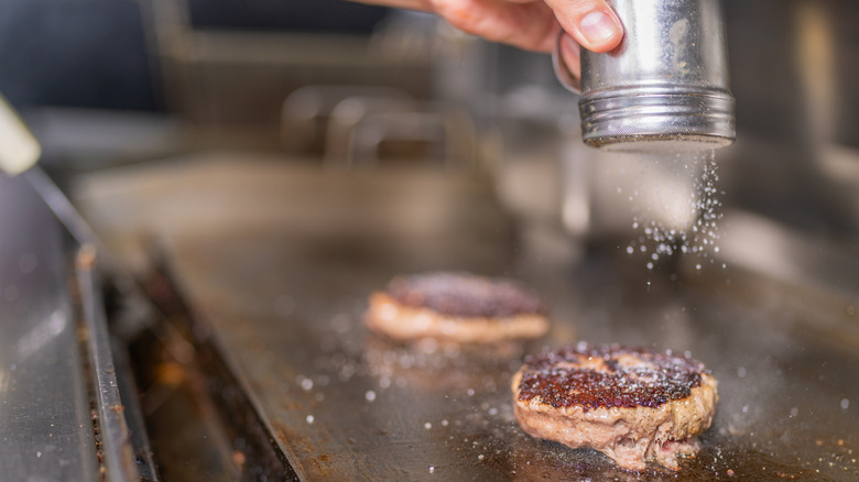 Cook adding salt to burger patties