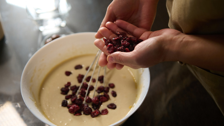 Hand putting dried fruit into a batter