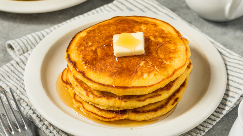 Stack of cornmeal-based pancakes with melting butter and syrup